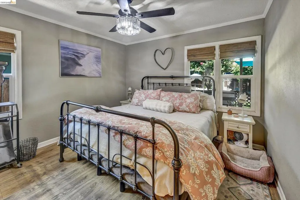 Bedroom featuring wood-finish flooring, a ceiling fan with integrated lighting, and two windows with woven shades