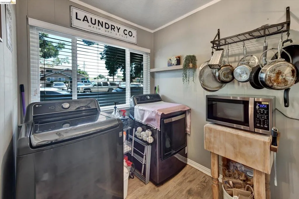 Laundry area featuring a large window with horizontal blinds, wood-finish flooring, and light-toned wall paneling