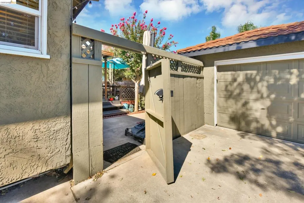 Paved side yard with a privacy gate, stucco exterior, and a garage with a roll-up door