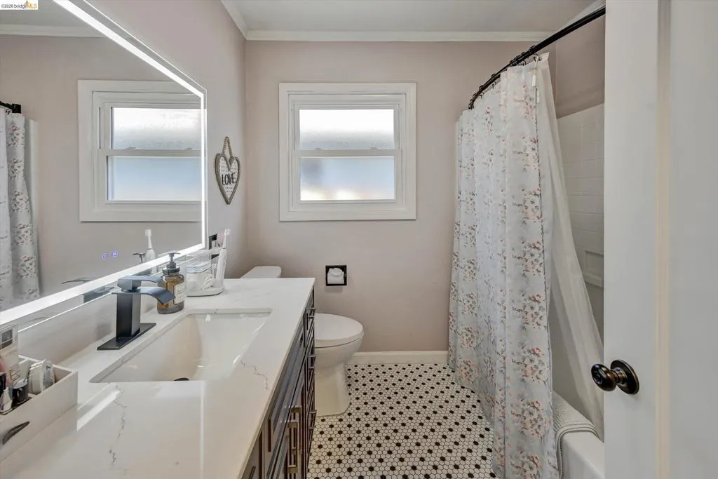 Bathroom featuring a vanity with a white countertop and integrated rectangular sink, a contemporary black faucet, an illuminated rectangular mirror, and black and white hexagon tile flooring