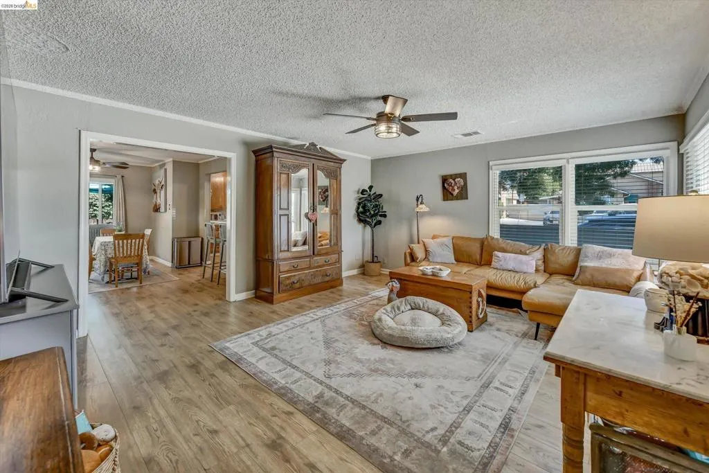 Living area with wood-finish flooring, light gray wall paint, and a ceiling fan with integrated lighting