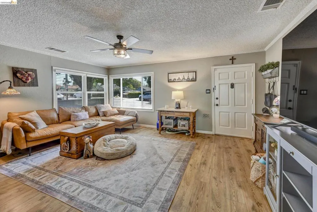 Spacious living area featuring wood-finish flooring, light grey wall paint, and multiple windows