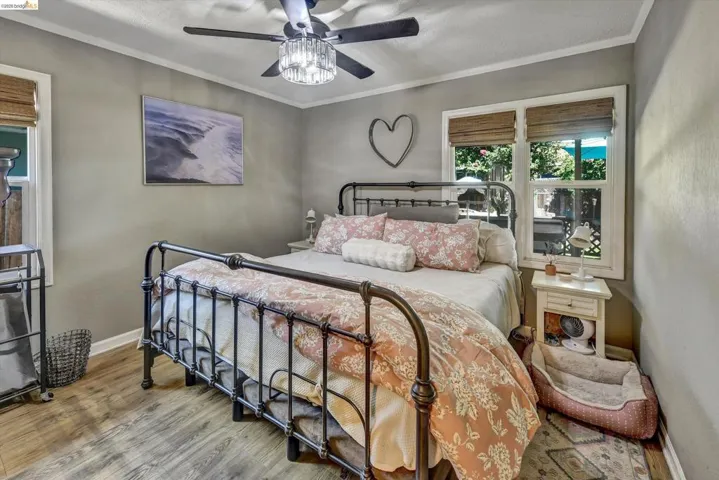 Bedroom featuring wood-finish flooring, a ceiling fan with integrated lighting, and two windows with woven shades