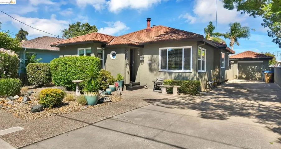 Stucco exterior with a terracotta tile roof, featuring a detached garage, concrete driveway, and front landscaping