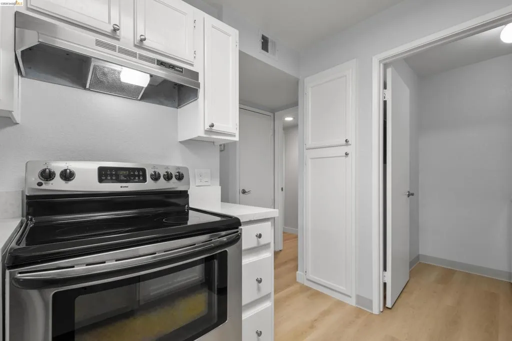 Modern kitchen featuring stainless steel electric range with dual ovens, white shaker-style cabinetry, under-cabinet lighting, and a brushed nickel range hood