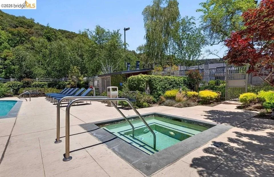 Resort-style backyard oasis featuring an in-ground spa with integrated handrails, sparkling pool, and expansive concrete patio