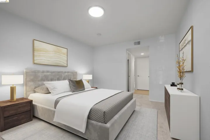 Spacious primary bedroom featuring a upholstered platform bed with gray linen headboard, dual nightstands with brass-accented table lamps, and a coordinating upholstered bench