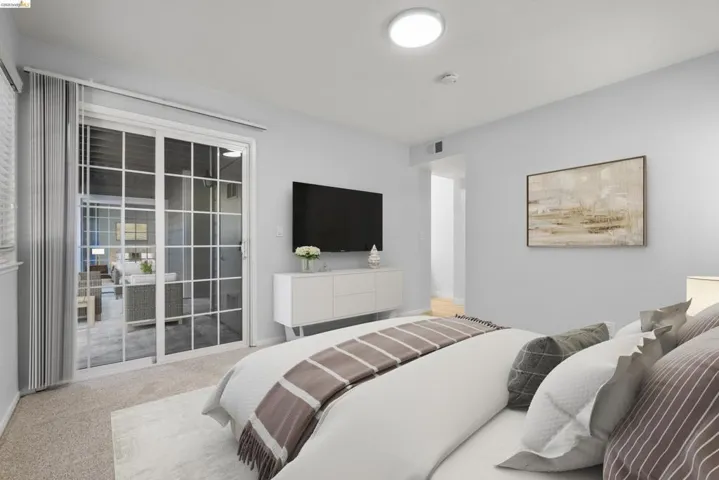Spacious bedroom featuring a wall-mounted flat-screen television, recessed ceiling lighting, and direct access to a sliding glass door with vertical blinds