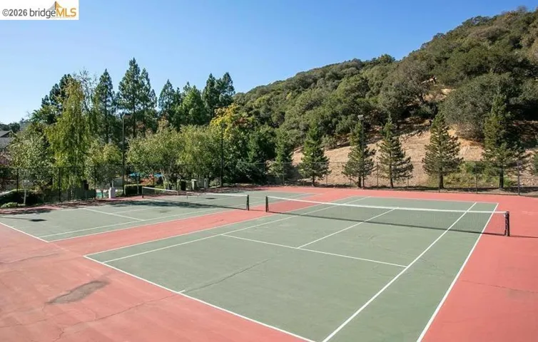 Professional-grade tennis courts featuring a well-appointed dual-court layout with regulation net systems, pristine hard court surfaces in contrasting red and green finishes, and white boundary line markings