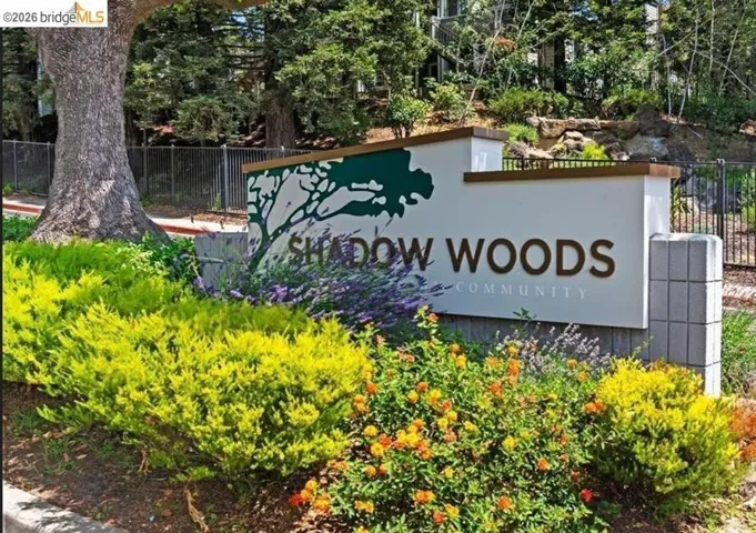 Community entrance sign featuring a decorative tree silhouette, block stone pillar, and surrounding shrubbery with colorful blooms