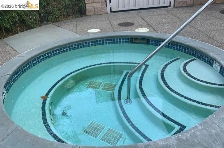 Circular spa with integrated tiered steps, blue mosaic tile trim, and an attached handrail