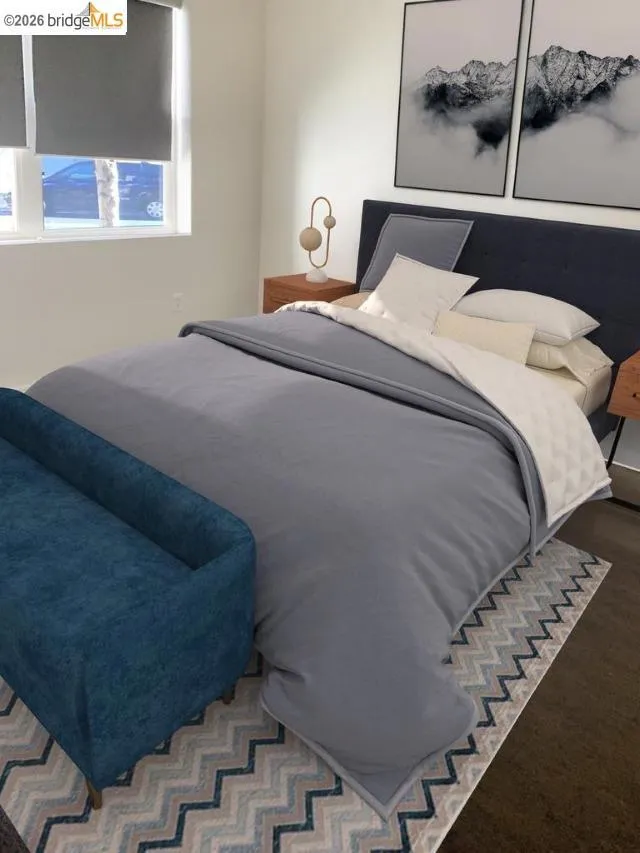 Bedroom featuring wood-finish flooring, white walls, and a window with roller shades