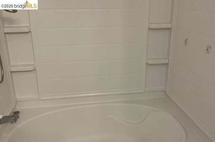 White built-in bathtub with integrated shelving and a chrome shower fixture