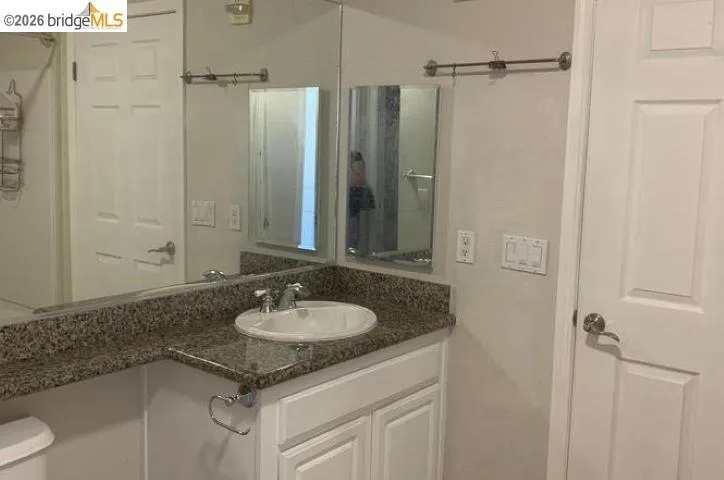 Vanity area featuring a granite-finish countertop, undermount sink, and white cabinetry