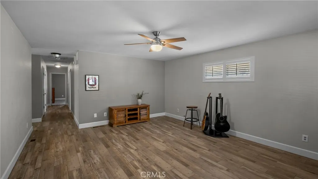 Living room with solid surface flooring, ceiling fan and windows with plantation shudders.