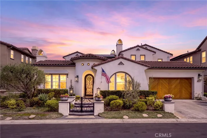Beautiful twilight view showcasing the home's timeless Spanish-inspired architecture, custom wrought iron entry gate, manicured landscaping, and inviting curb appeal within the prestigious gated community of Rancho Madrina.