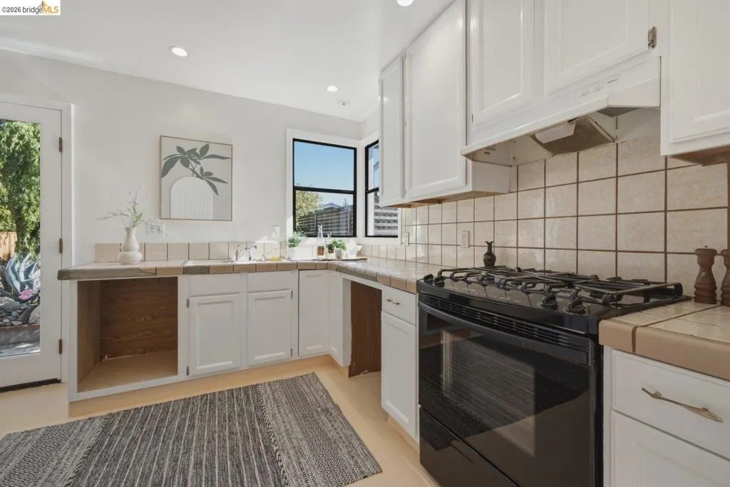 Bright kitchen featuring white cabinetry, tile countertops, a four-burner gas range with oven, a window above the sink, and recessed lighting