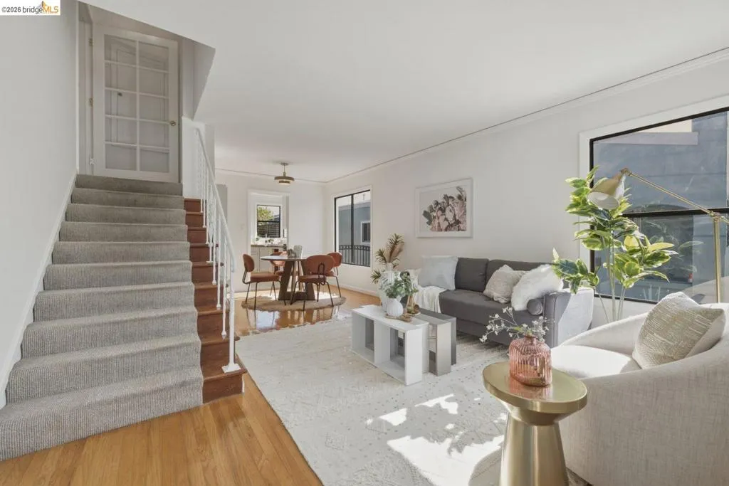 Living area featuring a carpeted staircase with white railings, hardwood flooring, and large windows