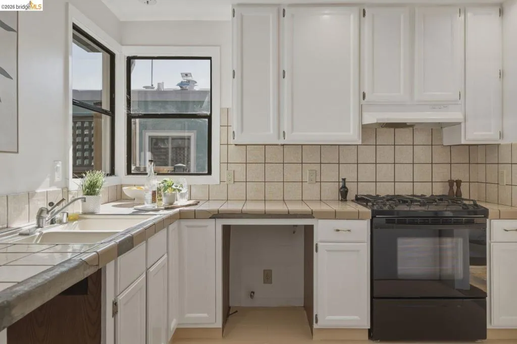 Kitchen featuring white cabinetry, tile countertops, a tile backsplash, and a black gas range