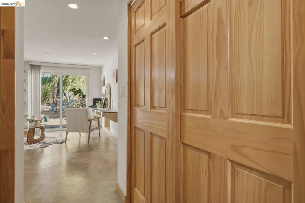 Paneled wood doors opening to an interior space featuring recessed lighting, a built-in wall desk, concrete flooring, and sliding glass doors leading to outdoor landscaping