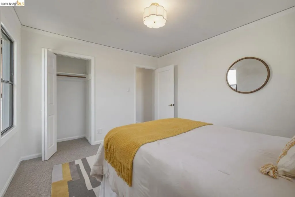 Room featuring light-colored carpet, a window with dark trim, a closet with bi-fold doors, a ceiling-mounted light fixture, and white wall paint