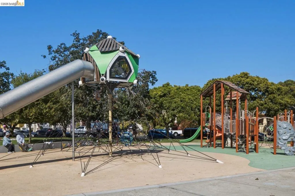 Outdoor play area featuring a large tube slide, a multi-level climbing structure with a green enclosure, rope climbing elements, and a separate wooden play structure with a slide