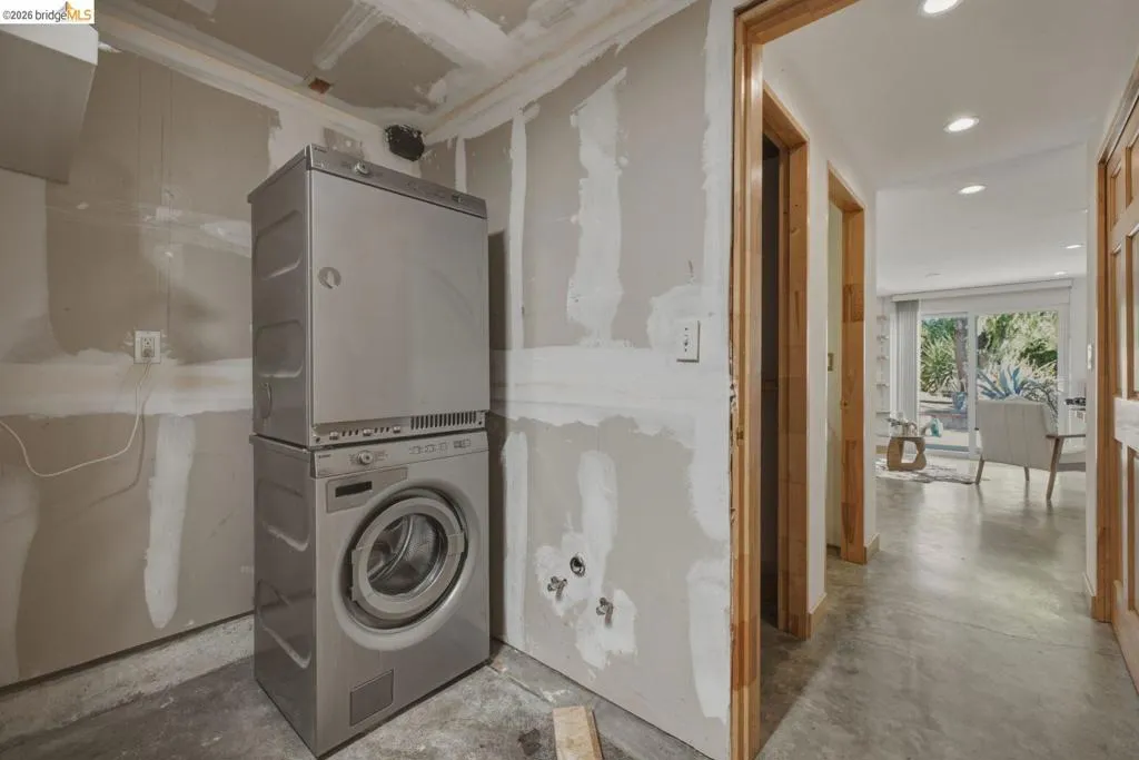 Utility area featuring a stacked washer and dryer unit, exposed drywall, and concrete flooring