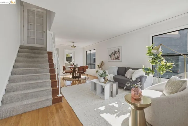 Living area featuring a carpeted staircase with white railings, hardwood flooring, and large windows