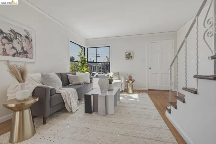 Light-filled living area featuring wood-finish flooring, a detailed panel door, and a staircase with an ornamental wrought-iron railing