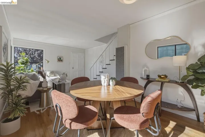Open-concept living area with wood-finish flooring, a contemporary round dining table, and a staircase featuring open risers and metal railings