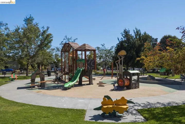 Expansive park area featuring a playground with multiple slides and climbing structures, surrounded by mature trees