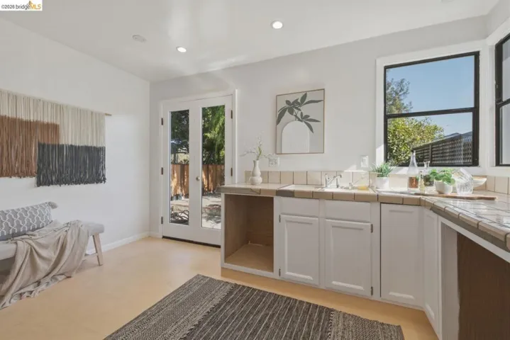 Kitchenette featuring tile countertops, white cabinetry, and a stainless steel sink
