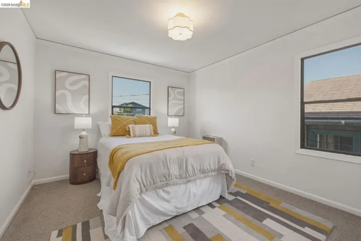 Bright bedroom with neutral wall paint and carpeting, featuring two windows with dark frames, and a flush-mount ceiling light fixture