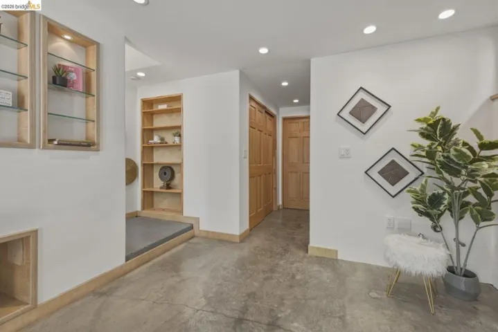 Concrete flooring with recessed lighting, built-in shelving, glass-front display cabinetry, and light wood trim