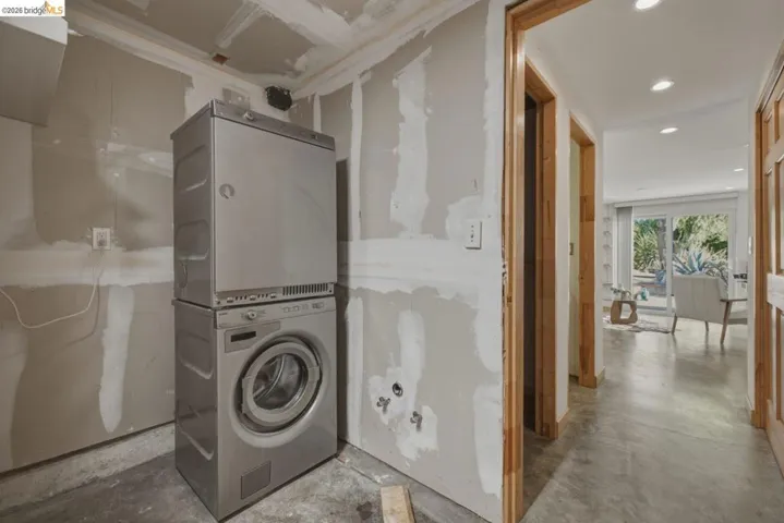 Utility area featuring a stacked washer and dryer unit, exposed drywall, and concrete flooring