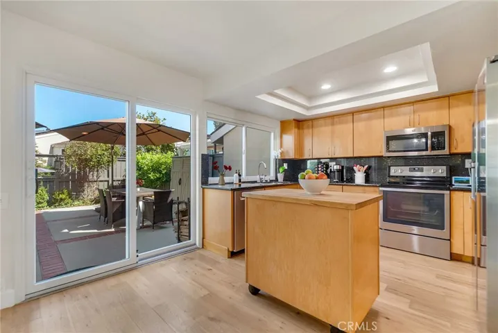 Remodeled kitchen with stainless steel appliances wooded cabinetry, mobile island, tray ceiling and dual pane sliders into back patio.