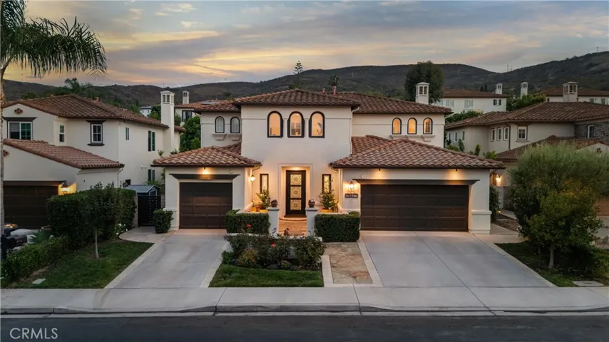 Mediterranean-style two-story home with stucco exterior, clay tile roof, three-car garage, arched windows, landscaped front yard, and private courtyard entry.