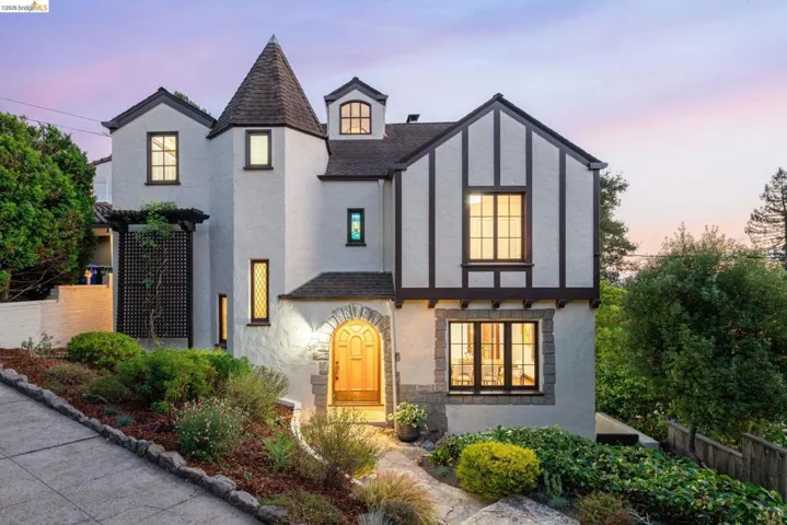 Tudor-style exterior with stucco and timber detailing, a stone archway leading to the entrance, a prominent turret, and a landscaped front garden with mature plantings