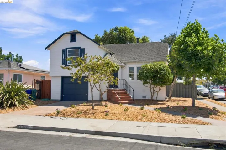 White exterior with dark blue shutters, attached garage, concrete driveway, and mature landscaping