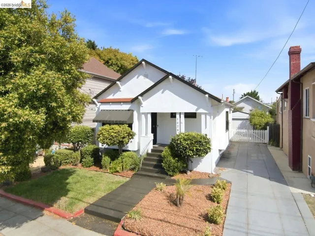 White exterior with black trim, covered entry, front lawn with landscaping, long driveway, and fenced rear yard