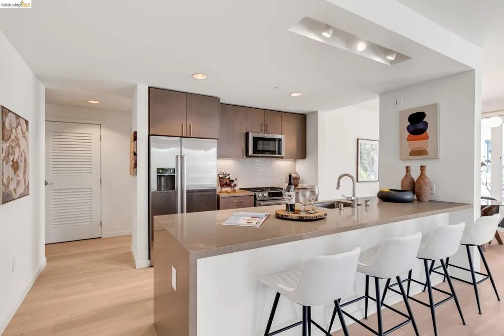 Modern kitchen featuring a breakfast bar with seating, integrated stainless steel appliances, wood-finish cabinetry, and recessed lighting