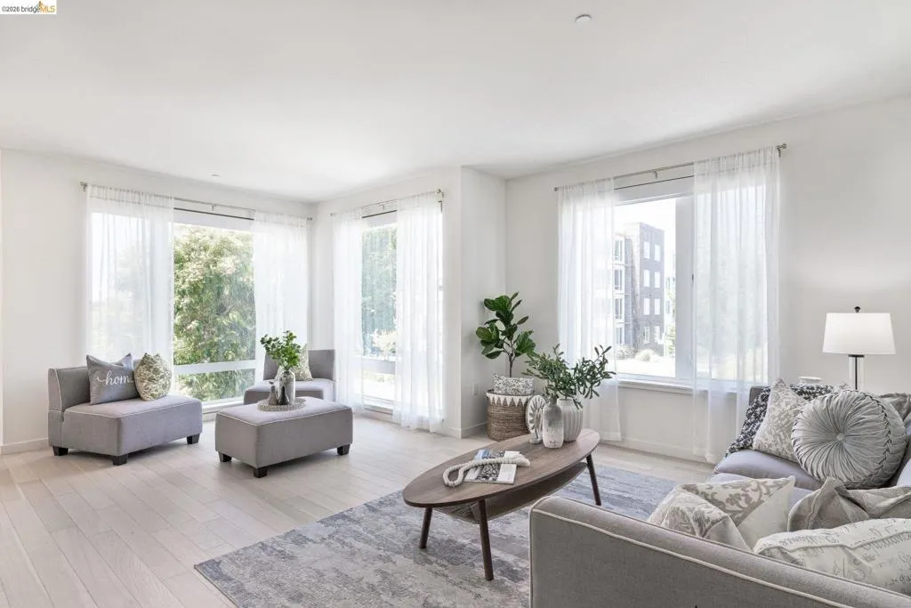 Expansive living area with large windows, light wood-finish flooring, and white walls