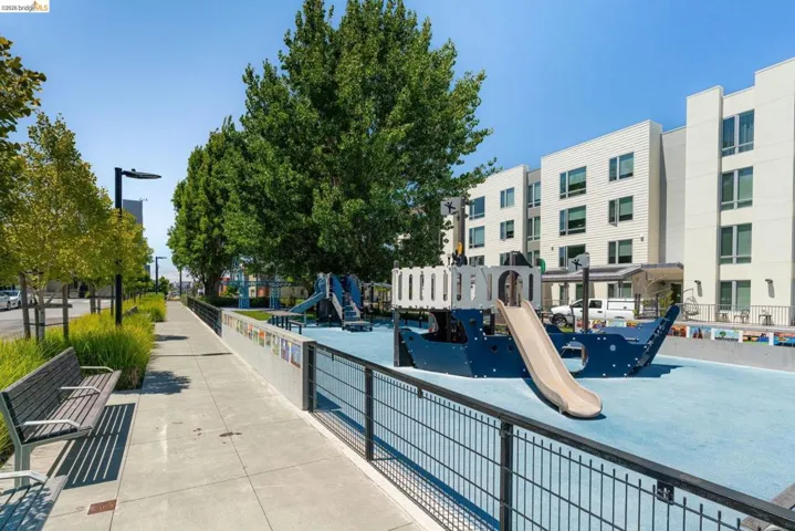 Playground area featuring a ship-themed structure with a slide, surrounded by a black metal fence