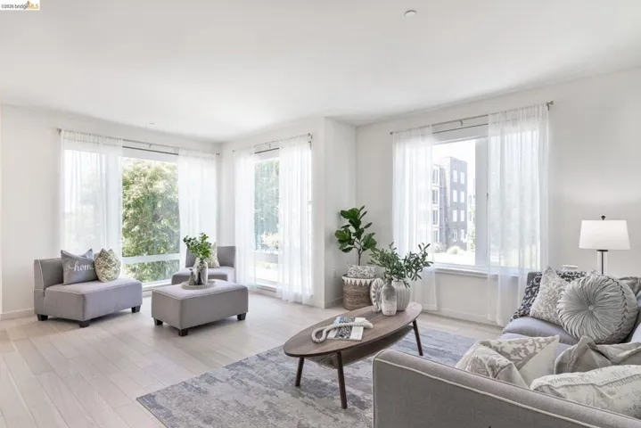 Expansive living area with large windows, light wood-finish flooring, and white walls