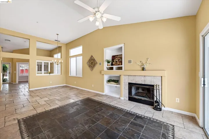 Vauted ceilings, tile flooring, built-in shelving, fireplace with tile surround, and an overhead ceiling fan