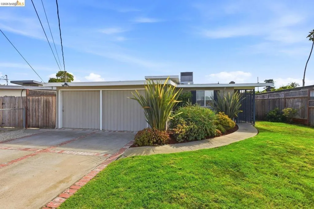 Contemporary single-story residence featuring an integrated garage, a concrete driveway with brick accents, and a well-maintained lawn