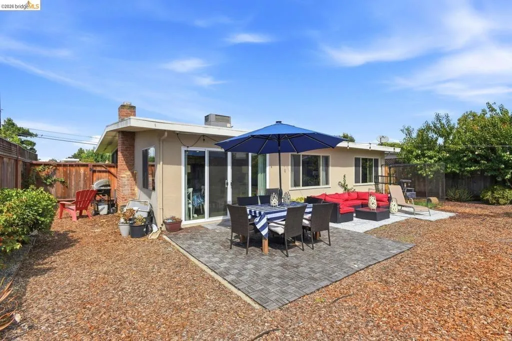 Expansive backyard featuring a large paved patio, secondary concrete patio, wood chip ground cover, mature landscaping, and privacy fencing
