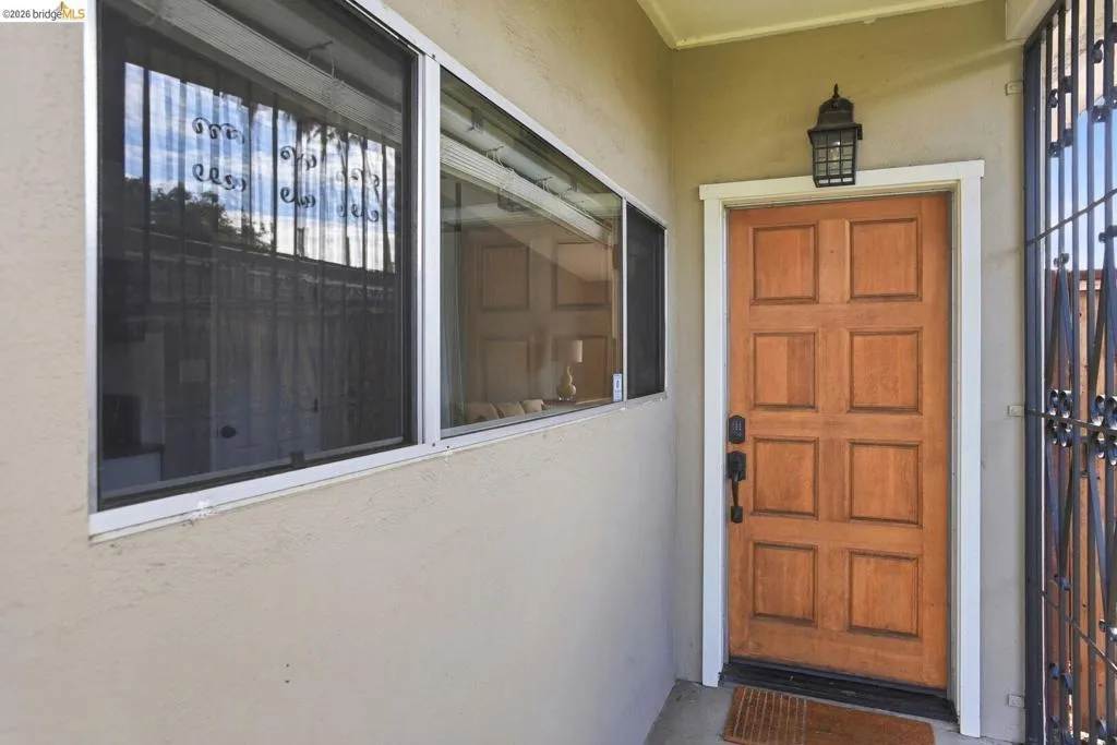 Wood paneled entry door with black hardware, electronic keypad, exterior wall lantern, and security window bars.