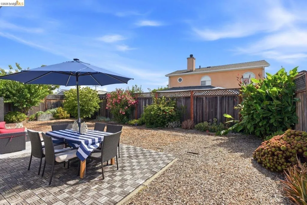 Spacious backyard featuring a tiled patio area, gravel landscaping, wood fencing, and mature plantings