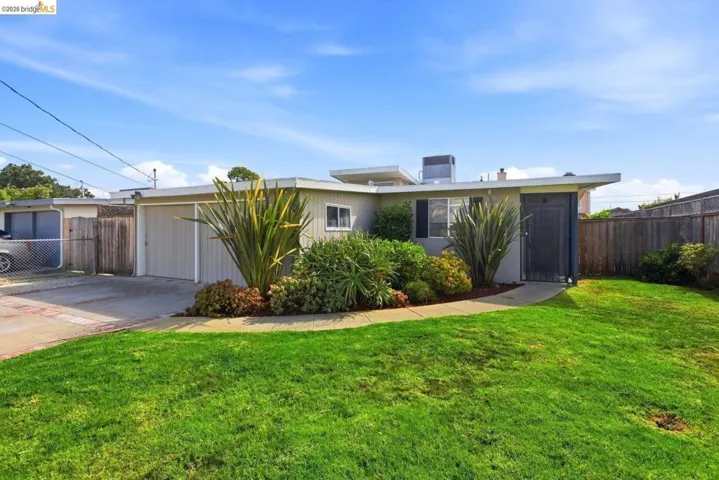Manicured front lawn, established landscaping, attached garage, concrete driveway, and a wood privacy fence